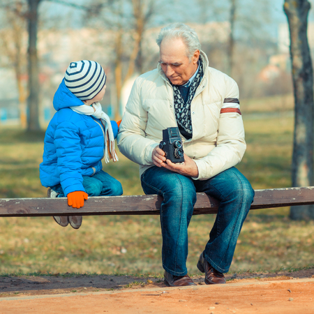 Grandfather and grandson are exploring vintage medium format cameras. Grandfather shows grandson retro cameraの写真素材