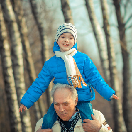Grandfather and grandson indulge. Grandfather Carrying Grandson On His Shoulders. The grandfather makes movies on old movie camera.の写真素材