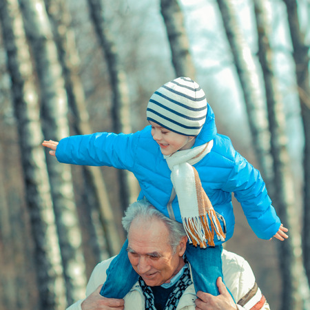 Grandfather and grandson indulge. Grandfather Carrying Grandson On His Shoulders. The grandfather makes movies on old movie camera.の写真素材