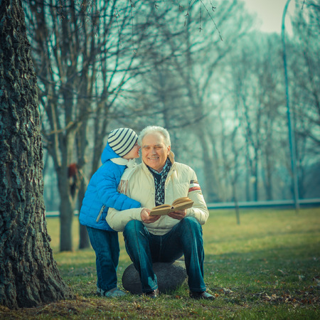 Grandfather and grandson reading a book outdoorsの写真素材