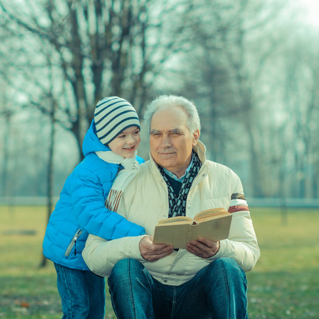 Grandfather and grandson reading a book outdoorsの写真素材