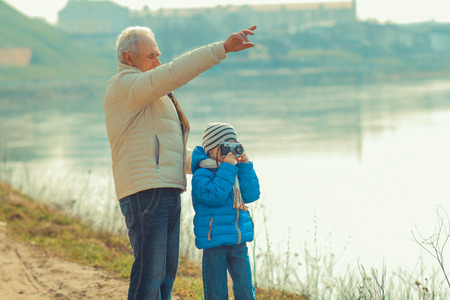 Grandfather and grandson are photographed on a vintage camera. Grandfather and grandchild in a landscapeの写真素材
