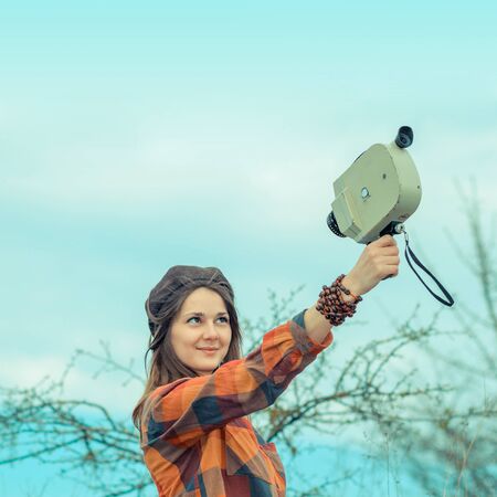 Hipster girl in a plaid shirt makes movies on a vintage movie camera.