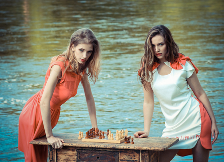 petite girls in a dress playing chess at a vintage table near the river. Vintage toningの写真素材