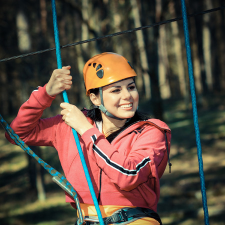 Beautiful girl in the outfit climbing climbs over obstacles between treesの写真素材