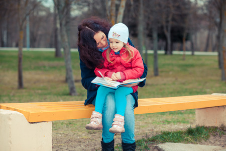 Mother with daughter read a book in the park. Happy young mother with her daughter at parkの写真素材