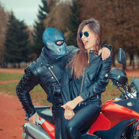 portrait of a beautiful hipster girl on a sports motorcycle with a guy in the skull maskの写真素材