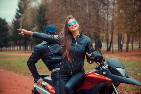 portrait of a beautiful hipster girl on a sports motorcycle with a guy in the skull maskの写真素材