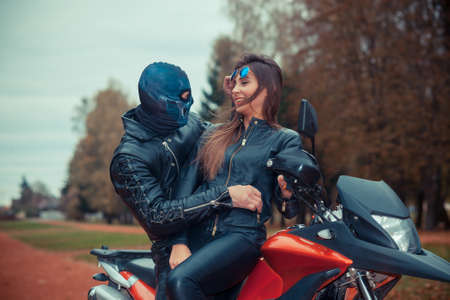 portrait of a beautiful hipster girl on a sports motorcycle with a guy in the skull maskの写真素材