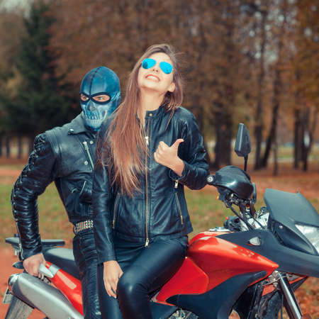 portrait of a beautiful hipster girl on a sports motorcycle with a guy in the skull maskの写真素材