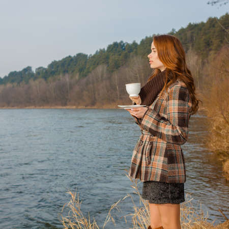 Romantic girl with cup outdoors. Hipster girl drinking tea in the spring in a landscapeの写真素材