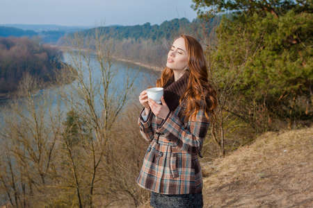 Romantic girl with cup outdoors. Hipster girl drinking tea in the spring in a landscapeの写真素材