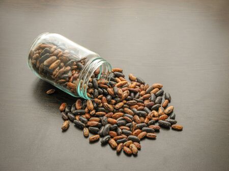 Short leg bean seeds (Phaseolus vulgaris) are poured from a glass jar on brown wooden surface. Bean seeds in a glass jar on the wooden table. Broad beans  in a glass dish.  These beans (Phaseolus vulgaris)  plant in northern Iran, Gilan provinc. In the local language, they call short leg broad bean. Wooden backgroundの写真素材