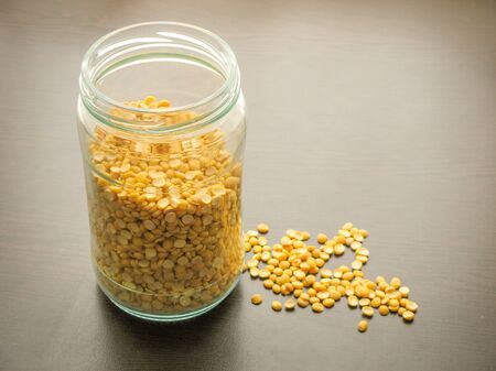 Yellow split dried peas in a glass jar on the wooden table. Yellow split dried peas in a glass dish. Wooden background. Yellow split dried peas are poured on wooden surface next to Yellow split dried peas in a glass jar. 
の写真素材