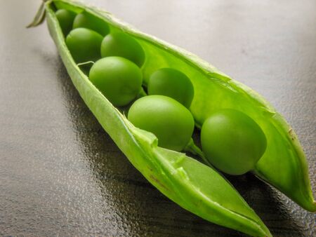 Green pea pod dark peas. Closeup of fresh green peas (Pisum sativum) in a glass jar on a wooden...