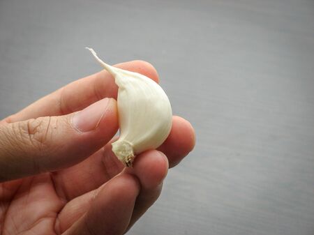Close up of single fresh white garlic clove on  fingers with table backgroundの写真素材