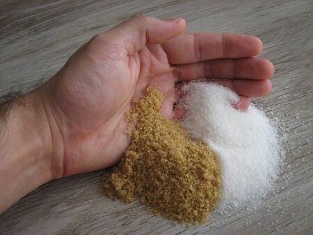 White and brown sugar on male hand with wooden background. Brown and white refined sugar.  Healthy and unhealthy concept. Close up.の写真素材