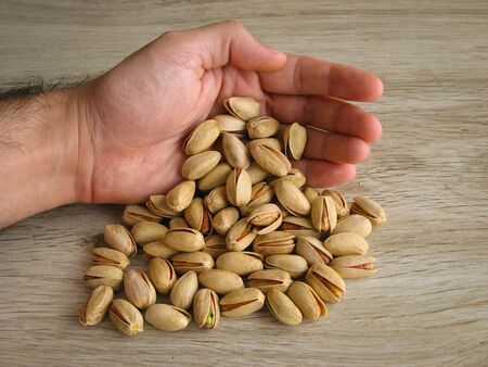 Dried organic pistachios in male hand on wooden background. Concept of vegetarian food. Healthy food. Full of protein and vitamin. Top Iranian pistachios.の写真素材