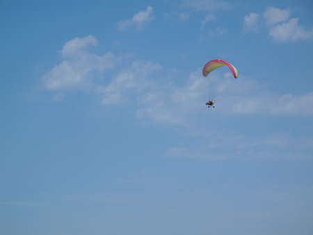 A paraglider flies in the sky under a multi-colored paraglider. paraglider flying under his wing in a blue sky. Performances on paraglidingの写真素材