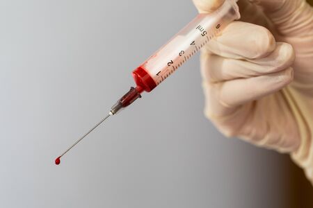 Syringe with a blood sample. A drop of blood at the end of the needle. Blood chemistry. Blood test for viruses.の写真素材