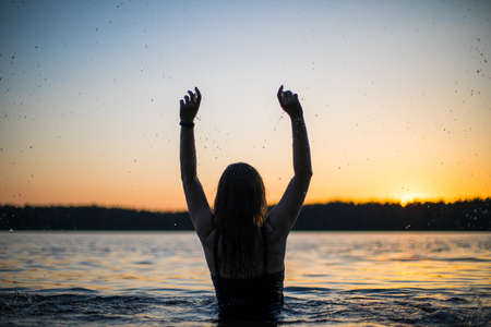 Beautiful Russian girl in a long black swimsuit swims outside the city on the lake in the rays of...