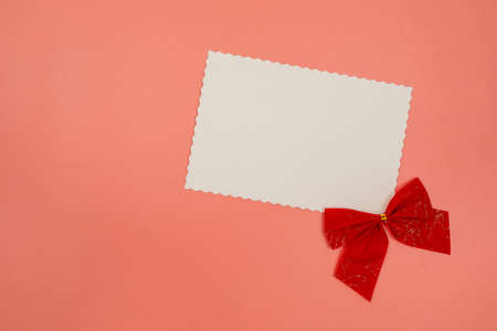 Blank white postcard and red bow decoration on pink background. Christmas, New Year, Valentines Day,...