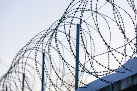 Sharp pointed razor wire barbed fence coiled on top of wall protects from prisoners and criminals in...