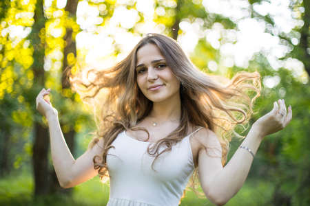 Beautiful young Russian girl dressed in a white dress, walks through the forest among the oaks in the rays of the sunsetの写真素材