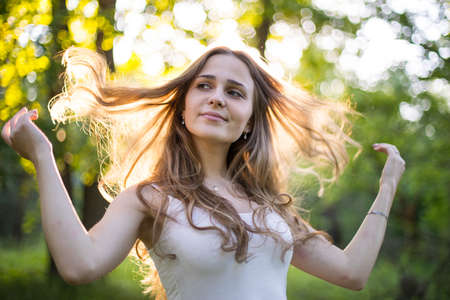 Beautiful young Russian girl dressed in a white dress, walks through the forest among the oaks in the rays of the sunsetの写真素材