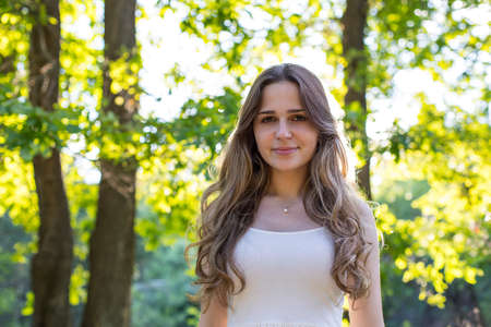 Beautiful young Russian girl dressed in a white dress, walks through the forest among the oaks in the rays of the sunsetの写真素材