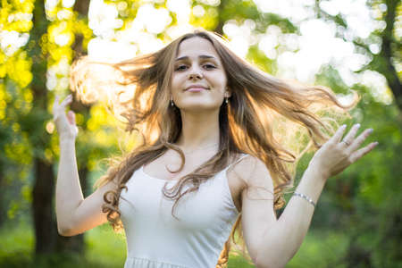 Beautiful young Russian girl dressed in a white dress, walks through the forest among the oaks in the rays of the sunsetの写真素材