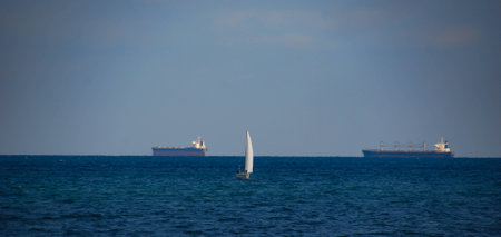 The sailing vessel is moving along the Black Sea, against the background of the blue sky, on the horizon there are transport ships on the roadsideの写真素材