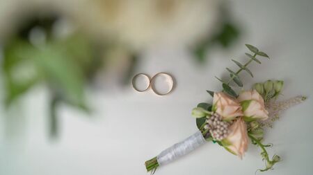 Wedding boutonniere and wedding rings on brown cloth.