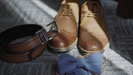 Close up of brown leather male shoes, bow tie, belt and camera on wooden background. Modern man or groom accessories. Wedding details. Male casual outfits. Top view, flat lay. Fees the groom. The morning of the groom. Boots, butterfly, beltの写真素材