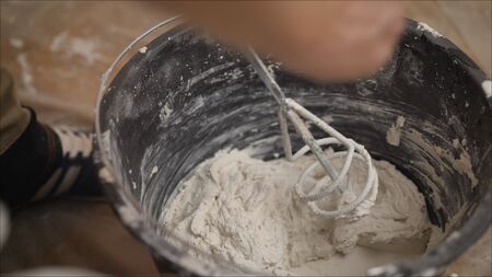 Builder mixes the mixture in a bucket using a construction mixer. Builder mixing plaster in a bucket...
