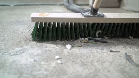 Preparing the floor for cover. The hand of a working man holds a broom, sweeping the concrete floor....