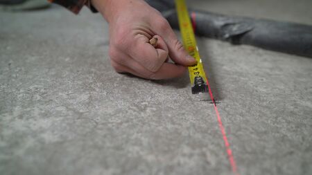 Floor repair. A worker with a tape measure makes marks on a concrete floor. the parquet master makes...