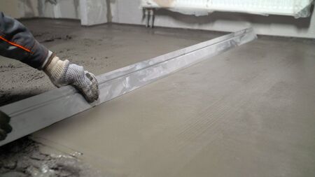 Construction work, concrete cement plaster. Using a spatula, level or level the concrete slab during the construction phase. The process of leveling floors in the apartment with a solution.の写真素材