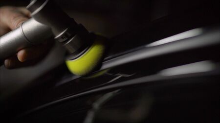 Car detailing - Hands with orbital polisher in auto repair shop. Selective focus.