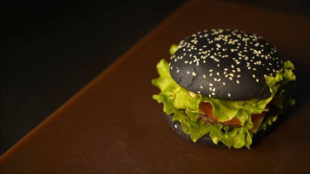 Concept of finishing cooking a black burger Burger with black buns. Sliced vegetables and meat. Taste the best hamburger. Black burger on the tableの写真素材