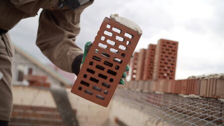 Bricklayer working in construction site of a brick wall. Bricklayer putting down another row of...