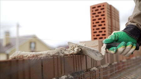 Bricklayer working in construction site of a brick wall. Bricklayer putting down another row of...