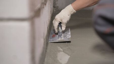 An industrial worker at a construction site installs a sealant for waterproofing cement. Worker puts liquid foil on a concrete floor. Workers applying the memory form of polymer waterproofing. Waterproofing the leveling floor with a spatula.の写真素材