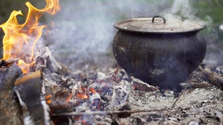 Cooking traditional soup over an open fire in the forest. Bonfire picnic in the forest. A pot of...