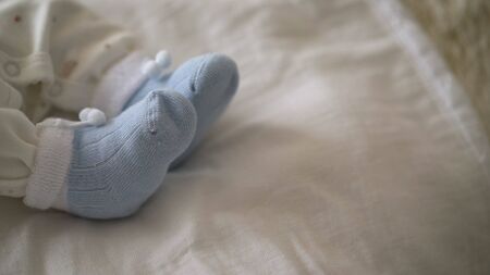 Tiny legs of the baby lie on a soft mattress, wear socks. Closeup of a young child in a home interior. Baby clothes concept. Newborn baby in blue socks.の写真素材