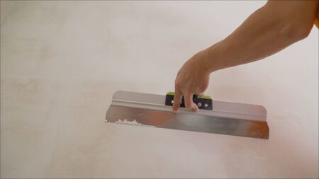 Construction worker with a long spatula plastering a wall. Worker aligns the wall with a spatula and...