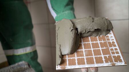 The master puts tiles on the wall. Master in overalls puts ceramic tiles on the wall