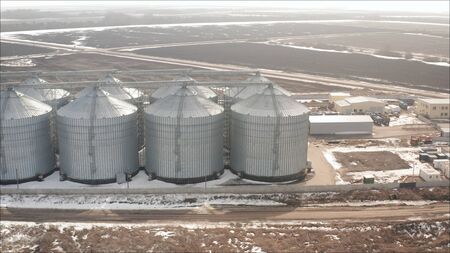Aerial view of drone on a large granary in a field on a background of a sunset. A new, built-in industrial grain elevator taken from a quadrocopter. An elevator for storing agricultural products in winter, general view.の写真素材