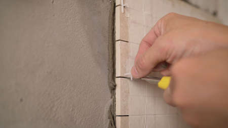 Close-up view of tiler hands fixing wall tile with spacers at home repair renovation work. Laying tiles on the wall.の写真素材