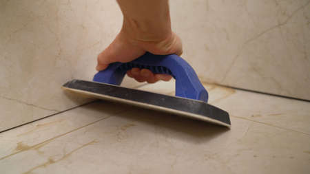 The hand of man holding a rubber float and filling joints with grout. The worker is rubbing the tiles with a float.の写真素材